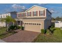 Two-story home featuring tan siding, red shutters, a brick driveway and an attached two-car garage at 613 Bloom Ter, Davenport, FL 33837