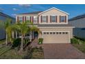 Two-story home featuring tan siding, red shutters, a brick driveway and an attached two-car garage at 613 Bloom Ter, Davenport, FL 33837