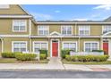 Inviting townhome showcasing a red front door, complemented by manicured bushes and classic white trim at 2602 Lodi Cir # 105, Kissimmee, FL 34746