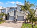 Modern townhome with a gray exterior, twin garages, decorative stone accents and well-maintained landscaping with palm trees at 635 Ocean Course Ave # 635, Champions Gate, FL 33896