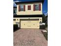 Two-car garage of a charming two-story home featuring red shutters and a brick driveway at 2523 Econ Landing Blvd, Orlando, FL 32825