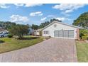 View of exterior with brick paver driveway leading to a two car garage with landscaped yard at 26913 Forest Hills St, Leesburg, FL 34748