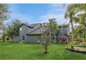 Expansive backyard with lush green lawn surrounds this gray two story house featuring tropical landscaping and mature trees at 2405 Abalone Blvd, Orlando, FL 32833