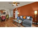 A living room with hardwood floors features an orange accent wall, gray couch and a ceiling fan at 3338 Robert Trent Jones Dr # 20804, Orlando, FL 32835