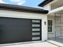 Modern home with a sleek black garage door featuring horizontal windows, adding a contemporary touch to the facade at 336 Caladium Ave, Lake Alfred, FL 33850