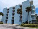 Exterior view of a blue condo building with multiple floors, balconies, tropical trees, and parking spaces at 4153 S Atlantic Ave # 1070, New Smyrna Beach, FL 32169