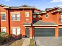 Townhouse featuring an attached garage, gray roof, and vibrant orange exterior paint at 142 Villa Di Este Ter # 204, Lake Mary, FL 32746
