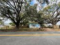 Charming blue house surrounded by large oak trees, featuring a white porch and fenced yard along the road at 9350 2Nd Ave, Orlando, FL 32824