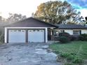 Single-story home with attached two-car garage featuring a mature tree in the front yard at 12314 Virginia Dr, Leesburg, FL 34788