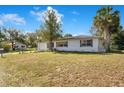 An expansive lawn surrounds this single story home with white siding and mature trees on a sunny day at 33 Sunset Dr, Debary, FL 32713