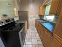 Galley kitchen featuring wooden cabinetry, black appliances, stainless refrigerator, and tile flooring at 1703 Doreen Ave, Ocoee, FL 34761