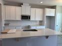 Bright kitchen with white cabinets, subway tile backsplash, stainless steel microwave, and an island with quartz countertop at 9338 Bolshoi Aly, Winter Garden, FL 34787