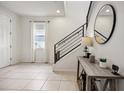 Bright foyer with neutral tile flooring, staircase with black railings, and decorative console table at 3953 Saltmarsh Loop, Sanford, FL 32773