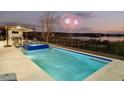 Inviting pool and hot tub area with outdoor dining and lounge seating overlooking a tranquil lake at twilight with fireworks at 14544 Avenue Of The Rushes, Winter Garden, FL 34787