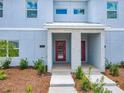 Inviting entrance to a modern townhome featuring a red door, fresh landscaping and a sidewalk at 2573 Reading Trl, Kissimmee, FL 34746