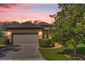 Charming single-story home with a brick driveway, two-car garage, and beautifully landscaped front yard at sunset at 556 Grande Dr, Davenport, FL 33837