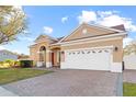 Angled view of the front of a tan home with a brick driveway and two-car garage at 8712 Irmastone Way, Orlando, FL 32817