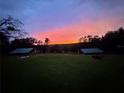 Backyard view features two sheds in the distance under a multicolored sunset sky at 13045 Mountain Trail, Clermont, FL 34715