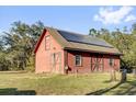 A well-maintained red barn with solar panels on its roof and large double doors at 11811 Kijik Trl, Groveland, FL 34736