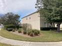 Side view of a two-story home with beige exterior, landscaping beds, and green lawn with sidewalk in front at 954 Lockbreeze Dr, Davenport, FL 33897