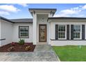 A modern home entrance with a unique wooden door, well-kept garden and black window shutters at 2480 Sw 147Th Lane Rd, Ocala, FL 34473