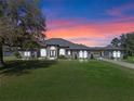 Picturesque single-story home featuring a long driveway, expansive lawn, and an elegant facade at sunset at 15523 Trotting Horse Ln, Tavares, FL 32778