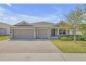Inviting single-story home with manicured lawn, mature landscaping, and a brick paver driveway leading to a spacious two-car garage at 103 White Horse Way, Groveland, FL 34736
