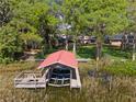 Aerial view of a boat dock with a red metal roof situated on the water, surrounded by lush trees and a well-maintained lawn at 35624 Cypress Ct, Leesburg, FL 34788