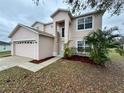 View of the two story home with a two car garage, manicured landscaping, and light pink exterior paint at 607 Kissimmee Ln, Kissimmee, FL 34759