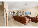 A living room with tile flooring and staircase access is furnished with a large brown leather sofa at 2508 Archfeld Blvd, Kissimmee, FL 34747