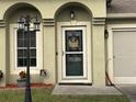 Close-up of the front door with decorative wreath, adjacent to the garage with updated lighting and lovely landscaping at 203 Flounder Pl, Kissimmee, FL 34759