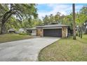 Ranch-style home with stone accents, dark gray garage door, long driveway and lush trees at 5374 Crooked Oak Cir, St Cloud, FL 34771