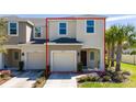 Two-story tan townhome featuring an attached garage, lush lawn, and a vibrant palm tree at 10849 Wyne Tree Ct, Orlando, FL 32824