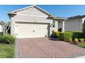 Beige two-car garage on a charming home with a brick driveway and neatly manicured landscaping at 17398 Blazing Star Cir, Clermont, FL 34714
