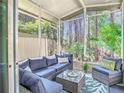 Relaxing screened porch with comfortable blue seating, glass table, and view of the beautiful trees in the backyard at 4952 Matteo Trl, Orlando, FL 32839