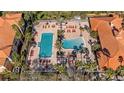 Aerial view of community pools and deck with lounge chairs, palm trees and terra cotta-roofed buildings at 5483 Vineland Rd # 10103, Orlando, FL 32811