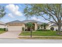 Charming one-story home with a well-manicured lawn, mature trees, and a brick-paved driveway leading to a two-car garage at 548 Burford Cir, Davenport, FL 33896