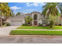 Two-story home featuring a manicured lawn, mature palm trees, a three car garage, and red front door at 13325 Falcon Pointe Dr, Orlando, FL 32837