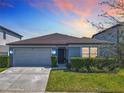 Well-maintained single-story home with a two-car garage and lush green front yard under a colorful sunset at 297 Citrus Isle Loop, Davenport, FL 33837