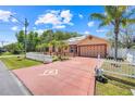 A ranch style home features mature palms, red driveway and a white picket fence on a sunny day at 449 Martigues Drive, Kissimmee, FL 34759
