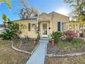 A quaint yellow home with vibrant landscaping, showcasing a welcoming walkway and charming architectural details under a sunny sky at 2107 University Dr, Orlando, FL 32804