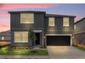 Modern two-story home with a gray exterior, black door and garage, and manicured lawn at twilight at 2306 Lancashire St, Davenport, FL 33896