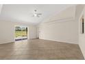 Bright living room with vaulted ceiling, ceiling fan, ceramic tile flooring, and sliding doors leading to backyard at 7847 Golf Paradise Way, Clermont, FL 34711