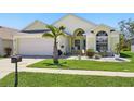 Charming, single story, yellow home with a manicured front lawn, palm tree, and two-car garage at 442 Troon Cir, Davenport, FL 33897