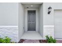 Stylish gray front door with a modern lantern, complemented by stone accents and lush landscaping at 4544 Windy Oak Way, St Cloud, FL 34772