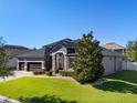 Gray house showcasing lush front lawn, stone entryway, and three-car garage at 16003 Tangerine Blossom Way, Winter Garden, FL 34787