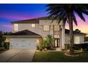 Dusk view of a two-story home featuring a lush lawn, a two-car garage, and elegant front entry at 12720 Greco Dr, Orlando, FL 32824