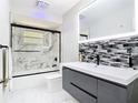 Modern bathroom with sleek gray vanity, stylish tile accent wall, and a glass-enclosed shower and tub at 9012 Notchwood Ct, Orlando, FL 32825