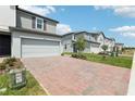 Attractive townhome showcasing a brick driveway, two-car garage, and neutral siding under a sunny, partly cloudy sky at 16450 Bird Of Paradise Ave, Clermont, FL 34714