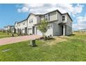 Attractive townhome showcases a brick driveway, lawn, and neutral siding under a sunny, partly cloudy sky at 16450 Bird Of Paradise Ave, Clermont, FL 34714